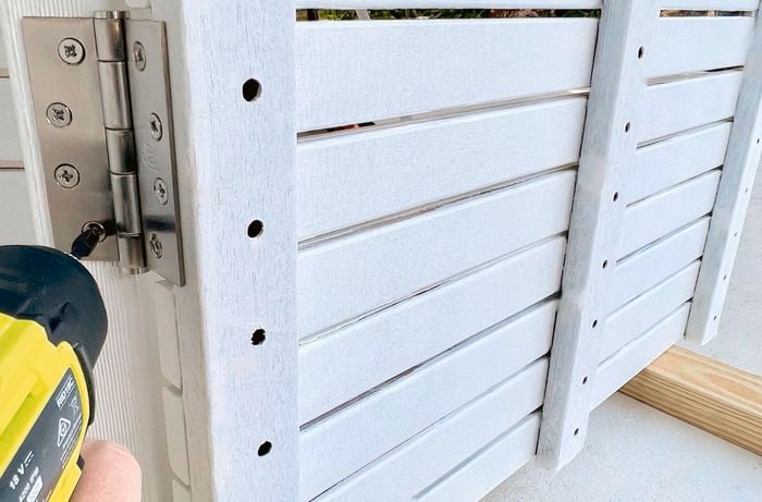 Person drilling a hinge to attach painted wooden panels.