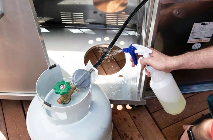 Spraying the fittings of a BBQ gas bottle with soapy water to detect leaks