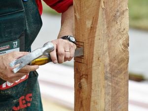 Person using hammer and chisel to cut out slots in fence post