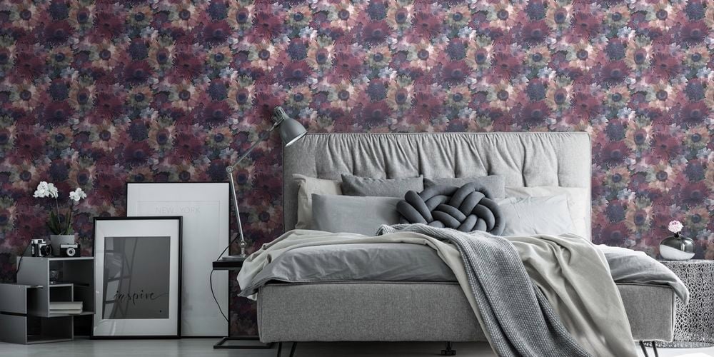 Bedroom with dark floral wallpaper, bed with furnishings, wall prints on ground and white round rug.
