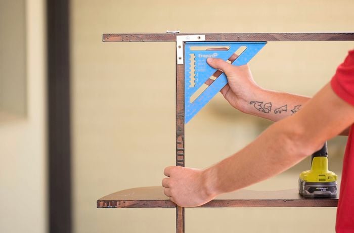 A person is adding brackets to the back of the bookshelf by securing all joints using screws.