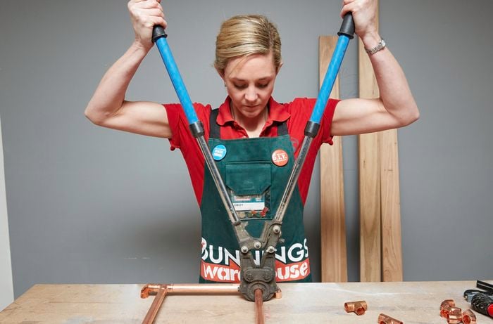 Person using crimping tool to connect copper pipe and copper joinery