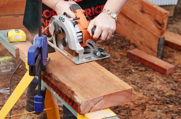 Pieces of timber to be used as gates for a sleeper compost bin being cut with a circular saw while held down with a clamp