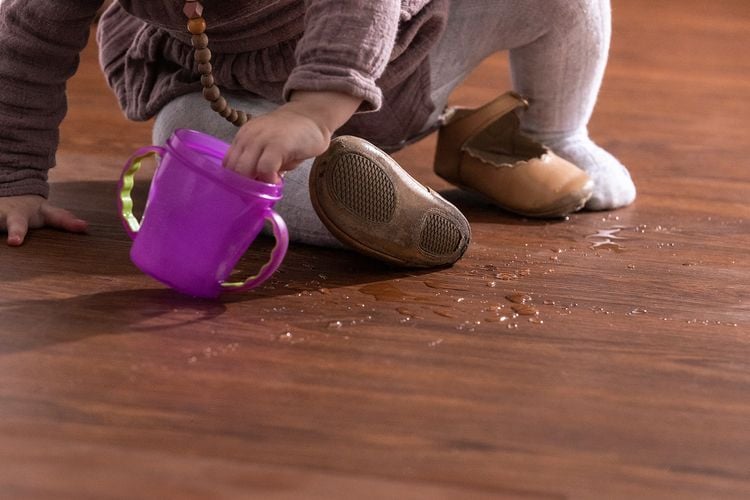 Close up of toddler spilling water from a cup onto vinyl plank timber-look floor