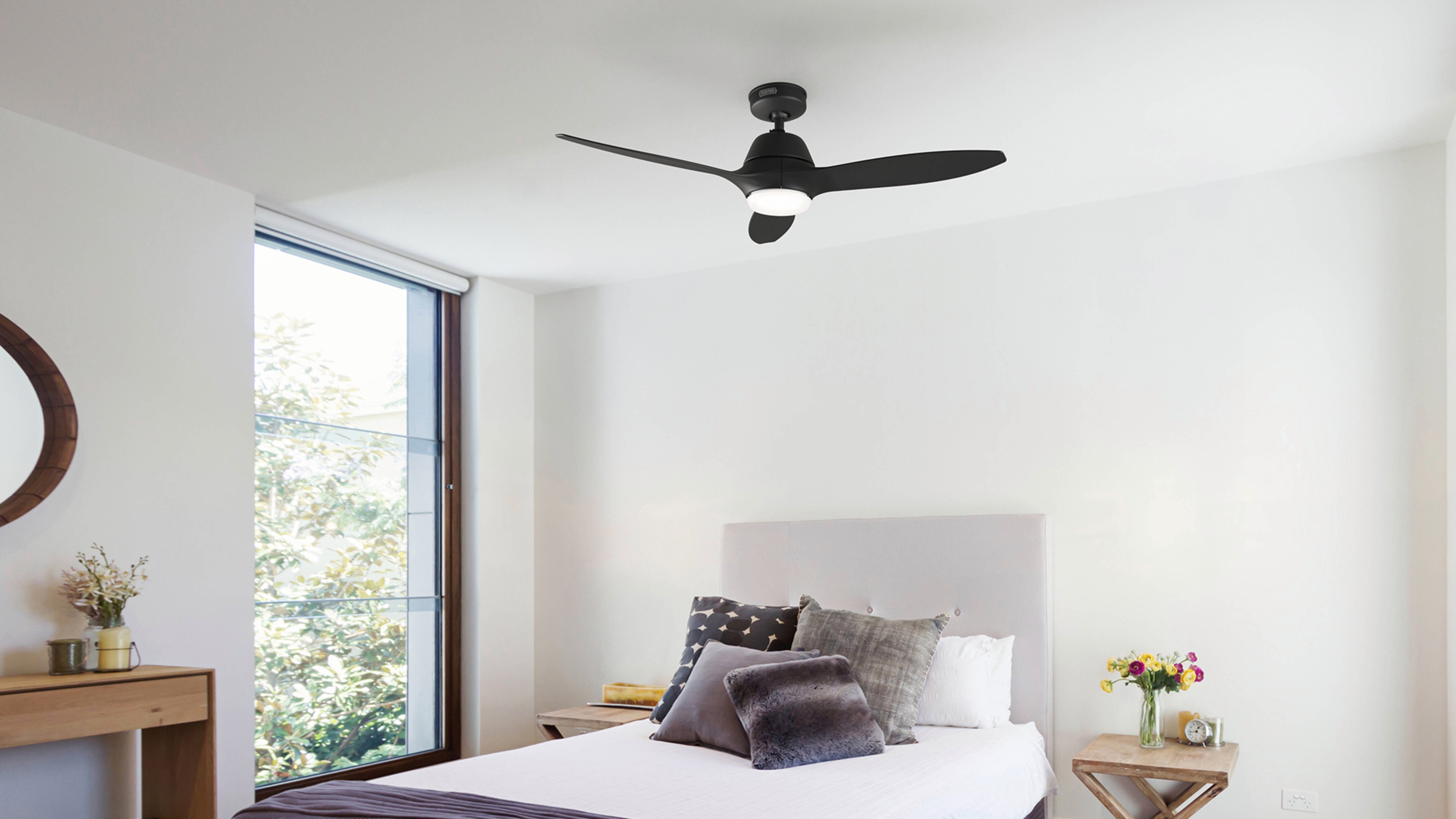 A black Calabasas ceiling fan with a light is installed in a bedroom with a bed, side tables and a large window.