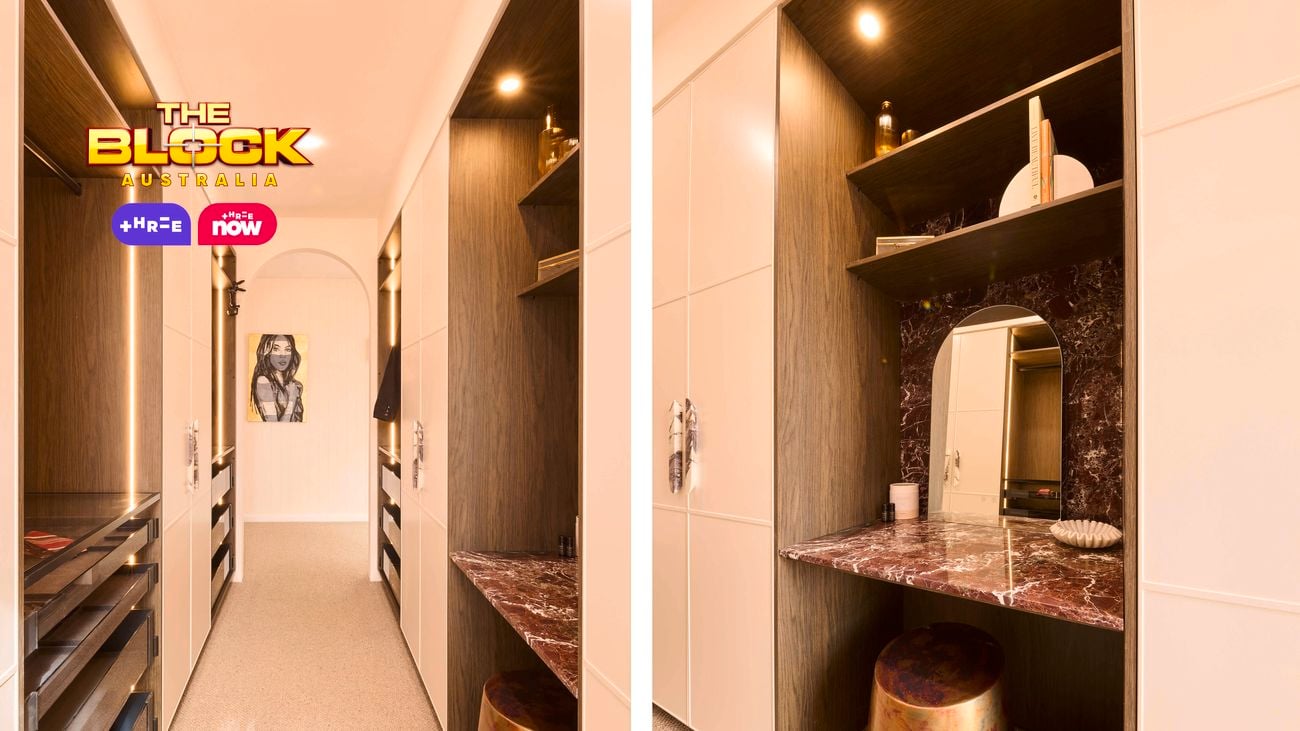 A modern walk-in wardrobe with light beige cabinetry and dark wood shelving. The space features integrated lighting along the shelves, a burgundy marble vanity on the right with a metallic stool, and multiple drawers on the left. At the end of the hallway, an arched doorway frames a wall with a monochrome portrait artwork. The floor is covered in neutral carpet, and the Block Australia logo appears in the top-left corner.