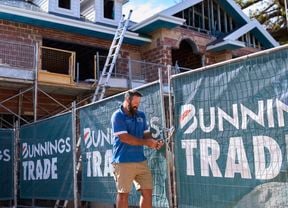 A man standing next to a fence on a trade site with Bunnings Trade signage on the fencing.
