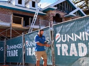 A man standing next to a fence on a trade site with Bunnings Trade signage on the fencing.