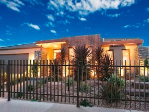 Grey fence sits in the front yard of a house, with outside lights on