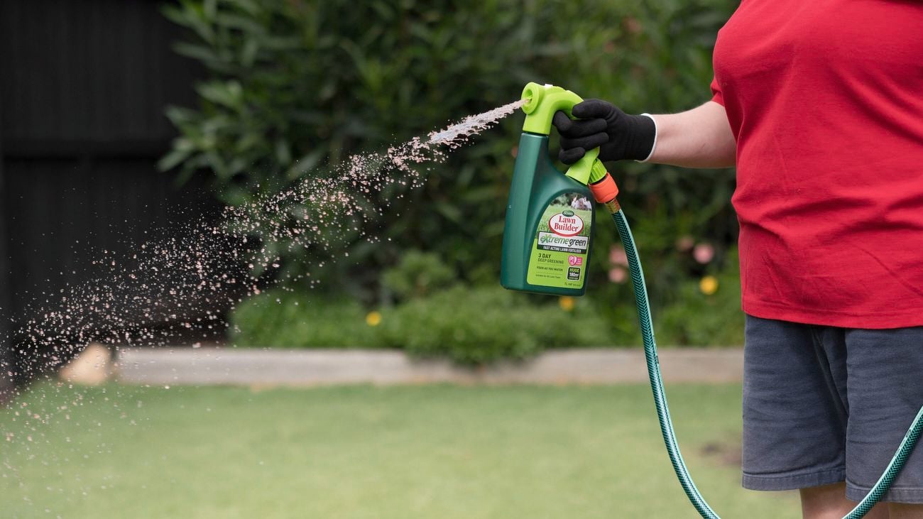 A person is distributing fast acting lawn fertiliser from Scotts through a garden hose.