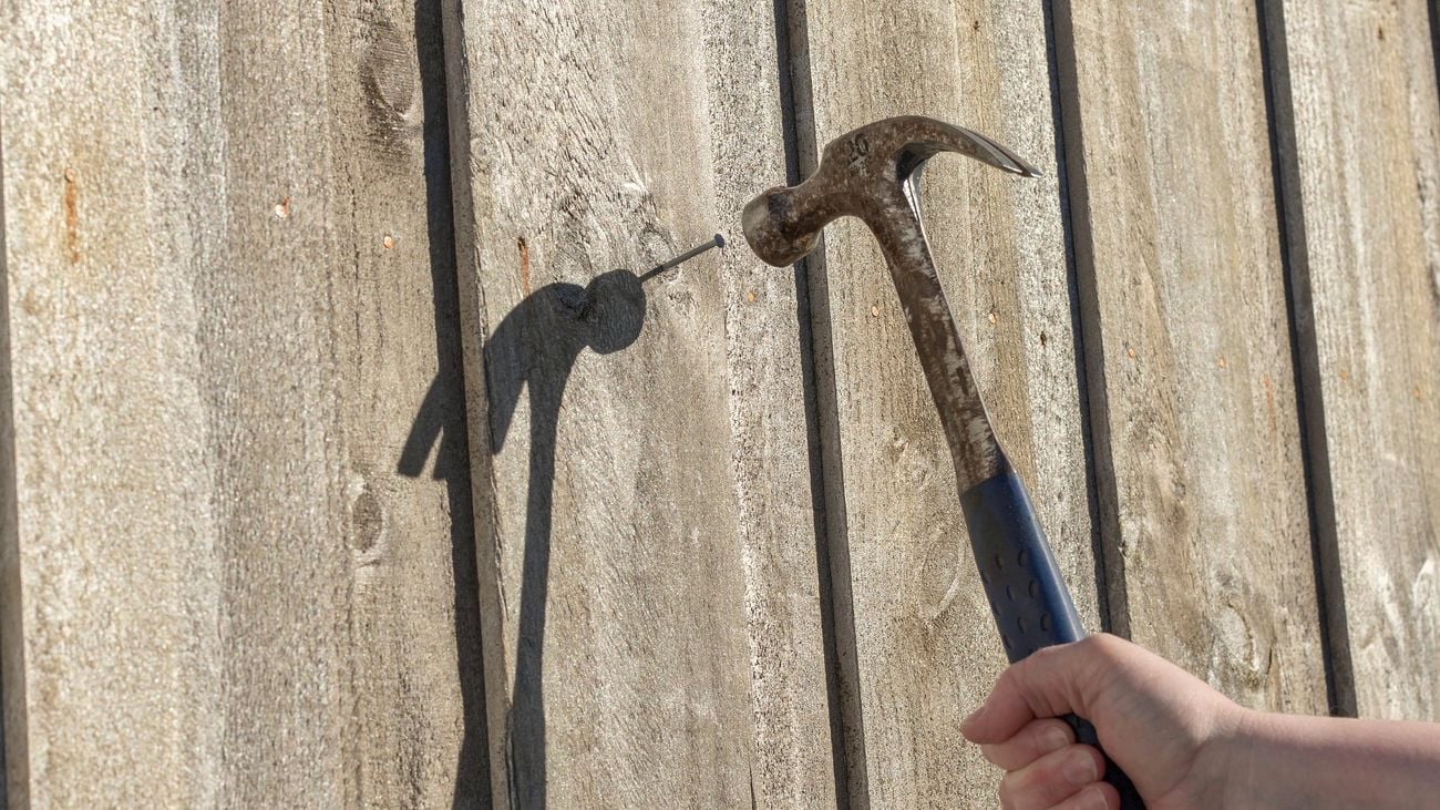 Person hammering a nail into a wooden fence.