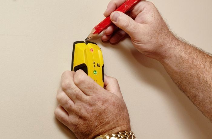 A person using a stud finder to mark a wall
