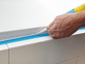 Person applying silicone sealant around the edge of a bath