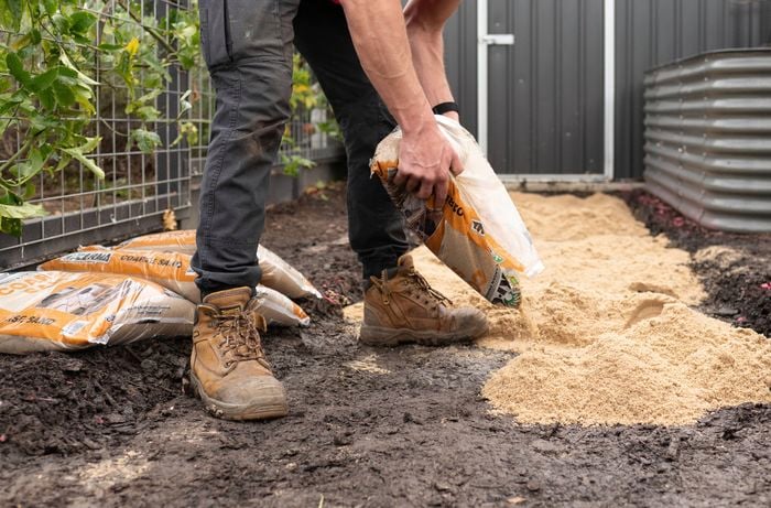 A person is pouring sand onto the dugout path. 