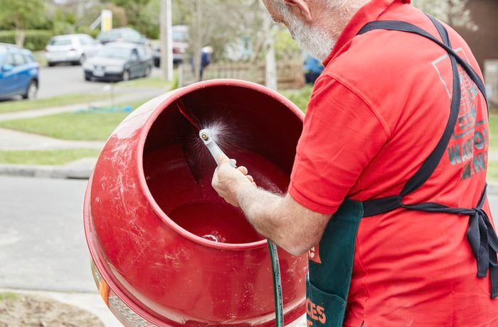 A person spraying water into a concrete mixer