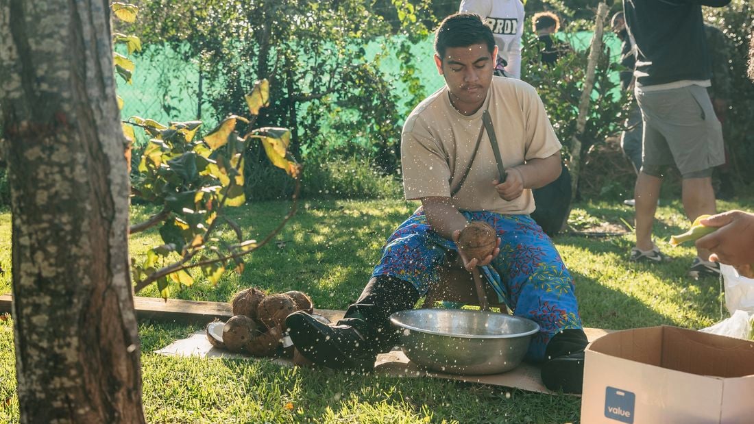 A man holding a coconut over a bowl outside