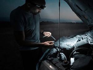 Man using light to fix car engine in dark 