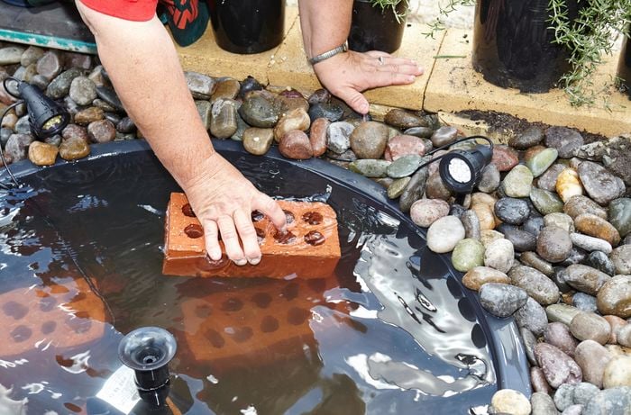 Person putting bricks into small pond feature.