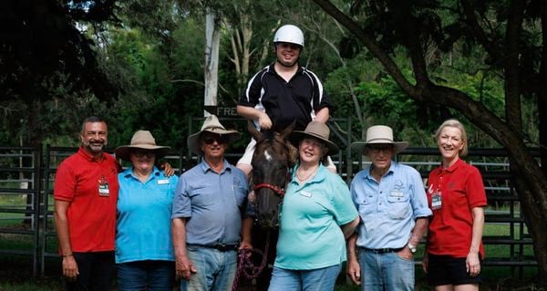 Two Bunnings Team Member's with other people standing next to a horse with a person on it outside.