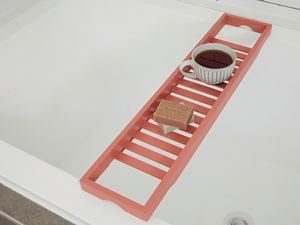 Painted bath caddy over bathtub with soaps and coffee cup.