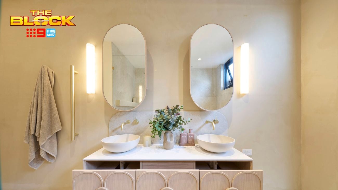 A modern bathroom with two sinks in it, with open drawers underneath these, two mirrors on the wall, a towel handing on a hook on the wall, and two lights on the wall.