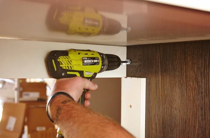 A person attaching parts of a cabinet using a cordless driver