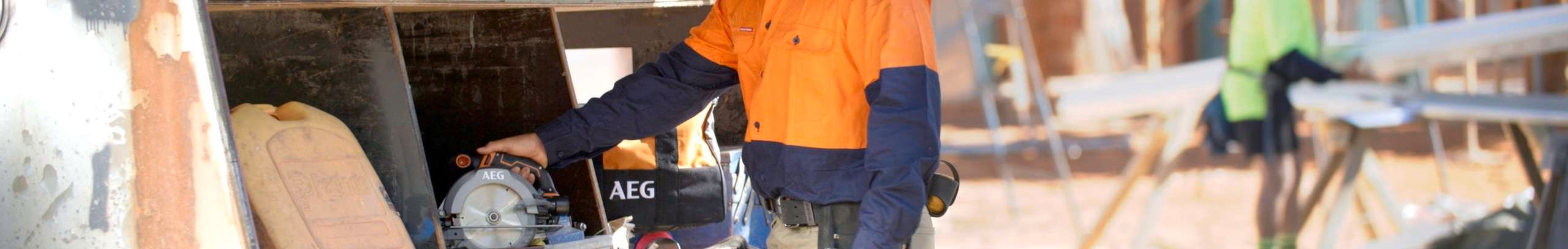 A tradie taking a saw out of a trailer on a work site.