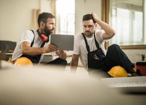 Two tradies sitting down at a worksite and looking at an iPad.