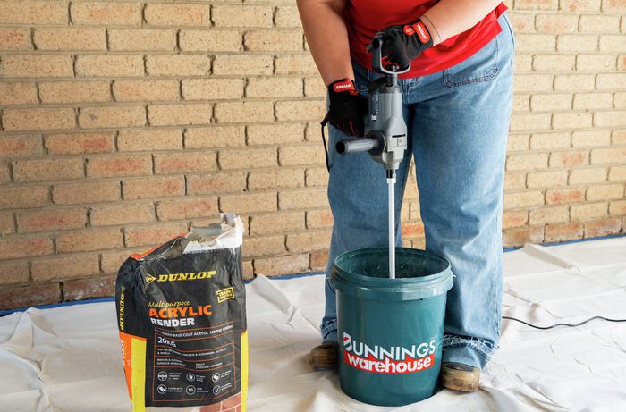 Person using drill and paddle to prepare render in bucket​​ 