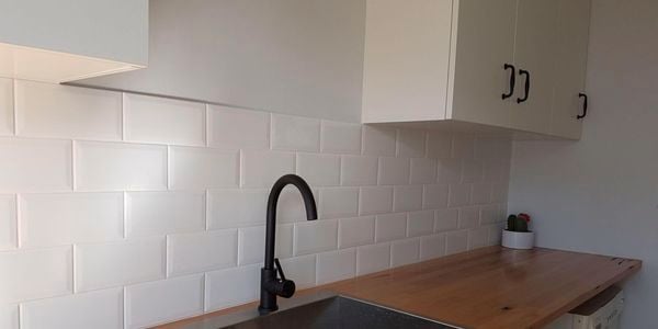 A laundry with white cabinets, timber benchtop and a black tap