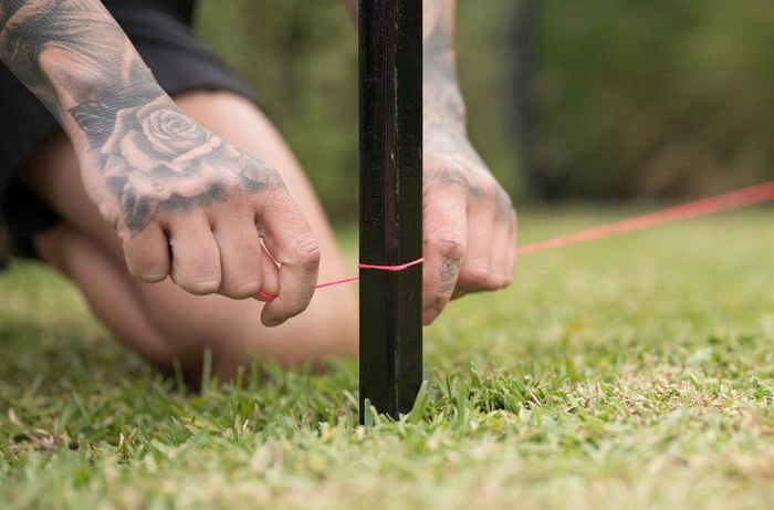 A person is attaching a string line around the stake in the ground to outline the perimeter for the garden bed.