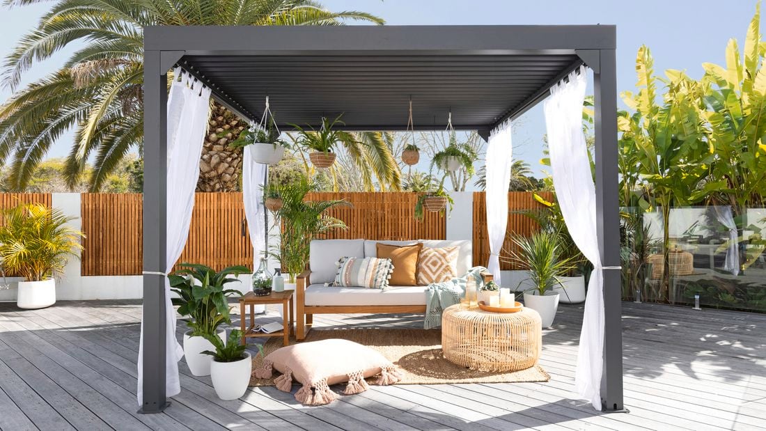 Outdoor gazebo styled with cushions, couch, hanging baskets and sheer curtains.