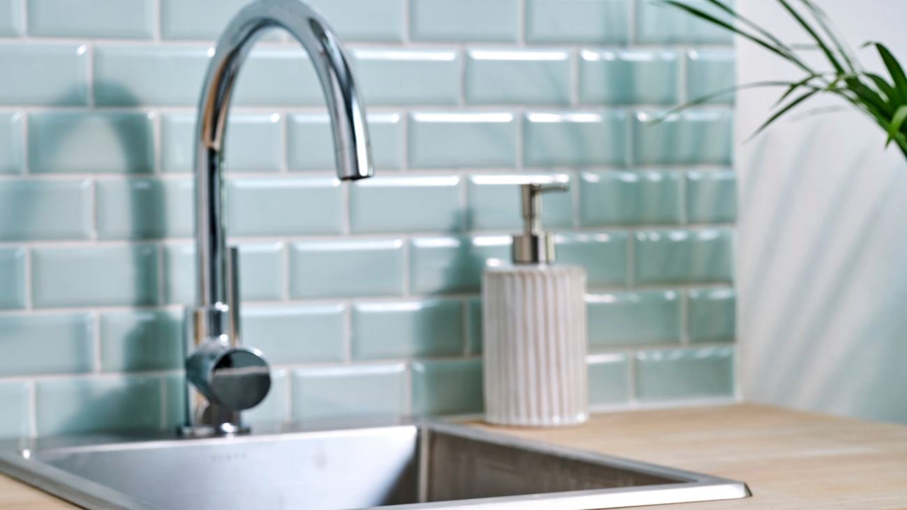 Close up of tiling, sink and soap dispenser