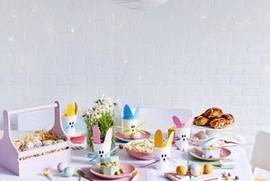 An Easter party table set up with painted eggs and hot cross buns