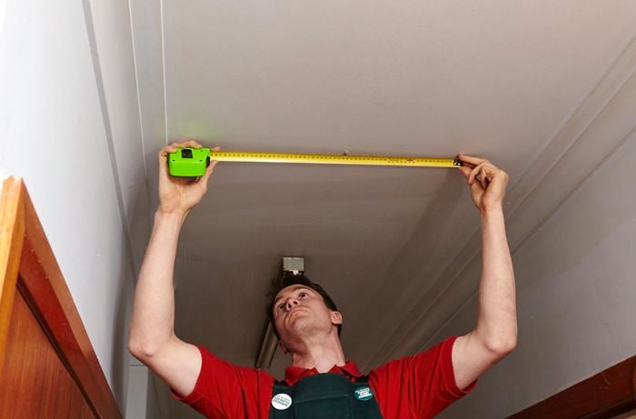 Person measuring hallway roof area with measuring tape.