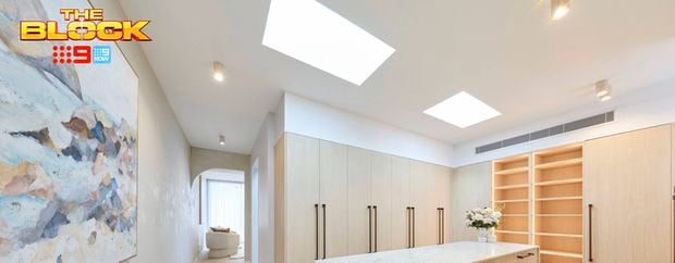 Spacious walk-in wardrobe with light timber cabinetry, central island drawers, open shelving, skylights and a large abstract artwork.
