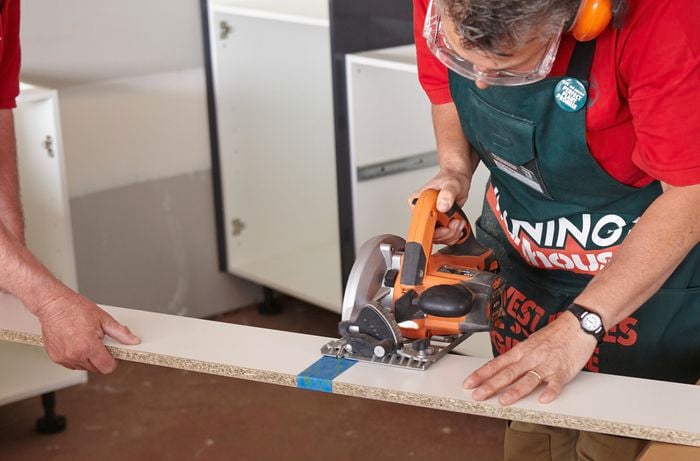 One person cutting a length of kickboard with a circular saw while another person holds the end