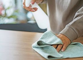 A person cleaning a wooden surface with a spray bottle and a cloth.