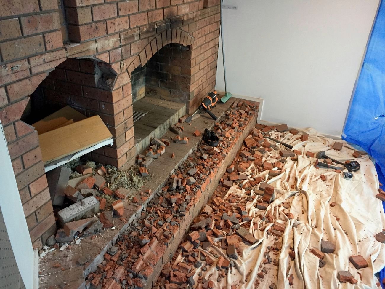 Partially demolished brick fireplace with debris and tools on white tarp during renovation.