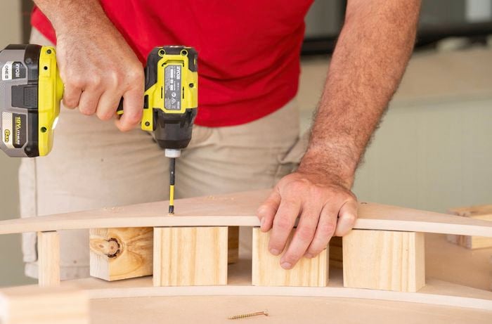 A person is using a drill to secure and MDF arch to wooden support blocks with screws.
