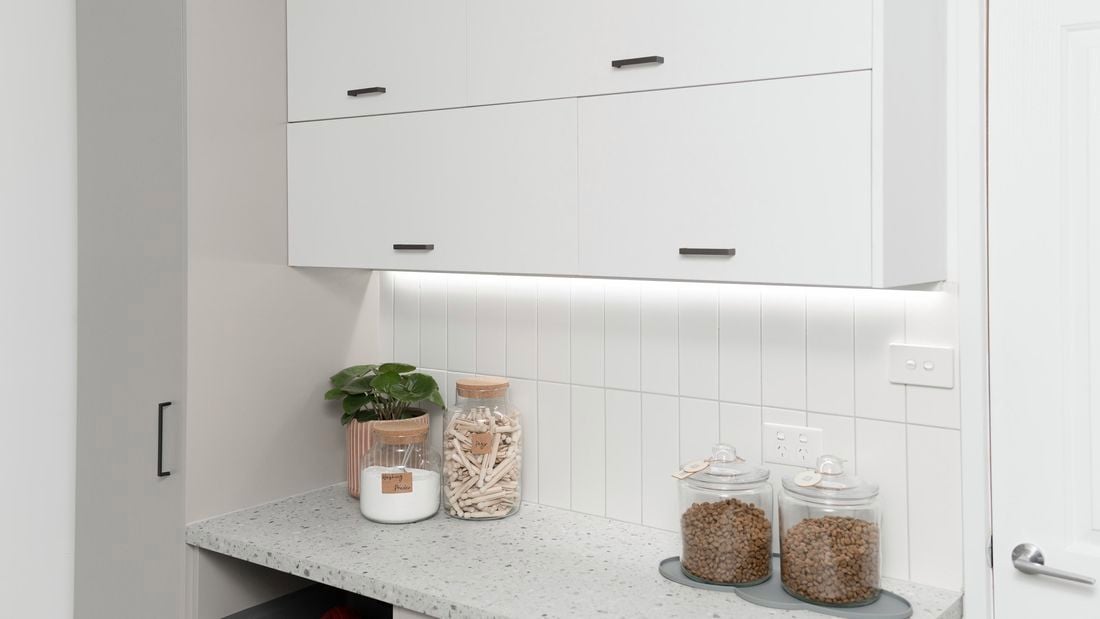 Laundry with lots of cupboards, jars for storage and a plant.