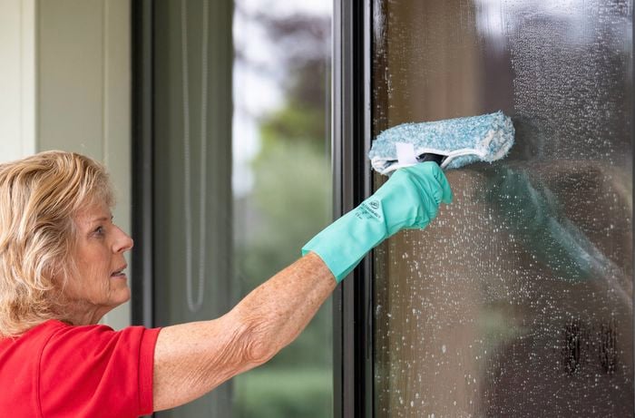 A Bunnings Team Member wearing gloves is cleaning a window using a window washer and cleaning solution.
