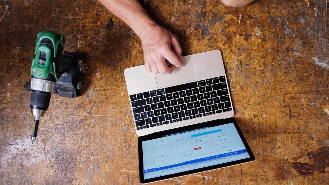 An image depicting a tradesperson using Xero accounting software on a laptop placed on a workbench, with a drill also in view. 