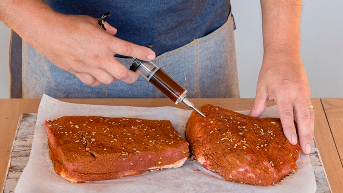 Person injecting meat with a marinade injector