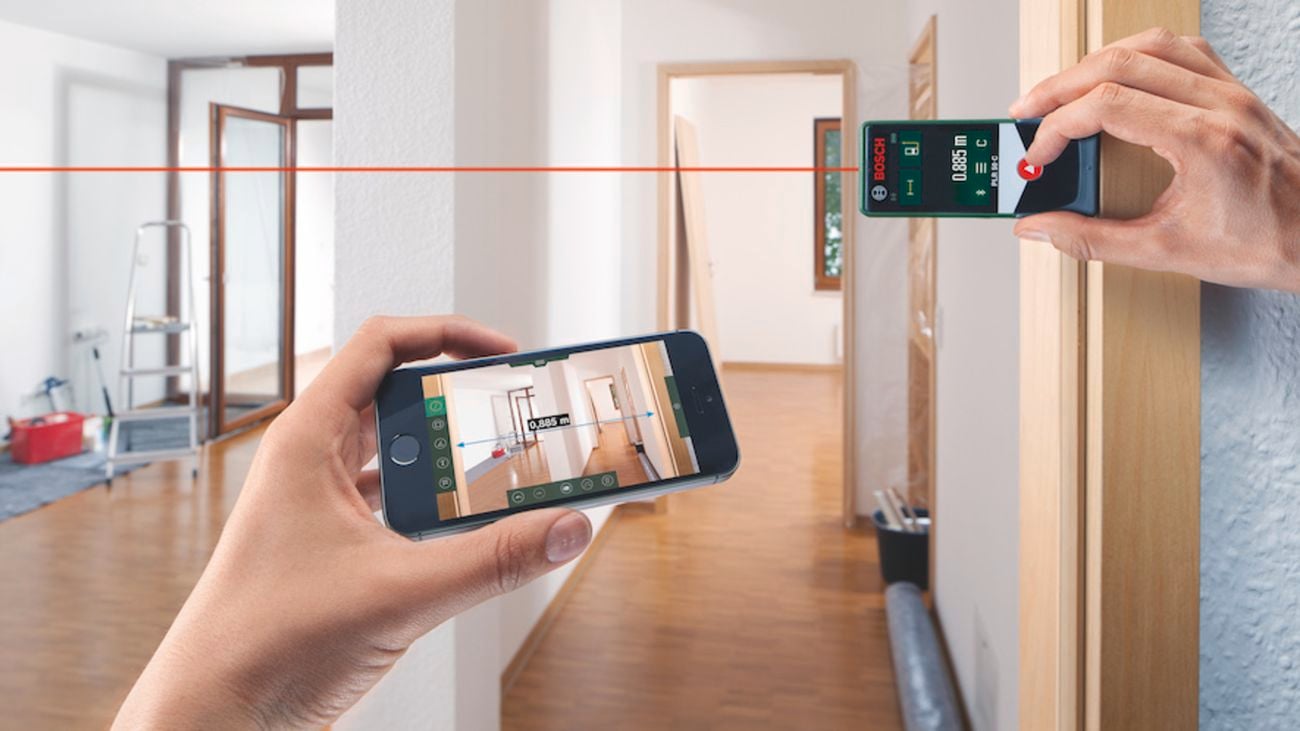 Hands holding a Bosch laser measure and smart phone in a house under construction.
