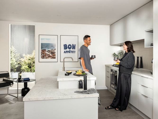 Couple standing in an oyster coloured kitchen drinking their morning coffee with a plate of scrambled eggs on the bench