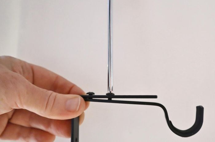 A person adjusts a curtain rod bracket before securing to wall