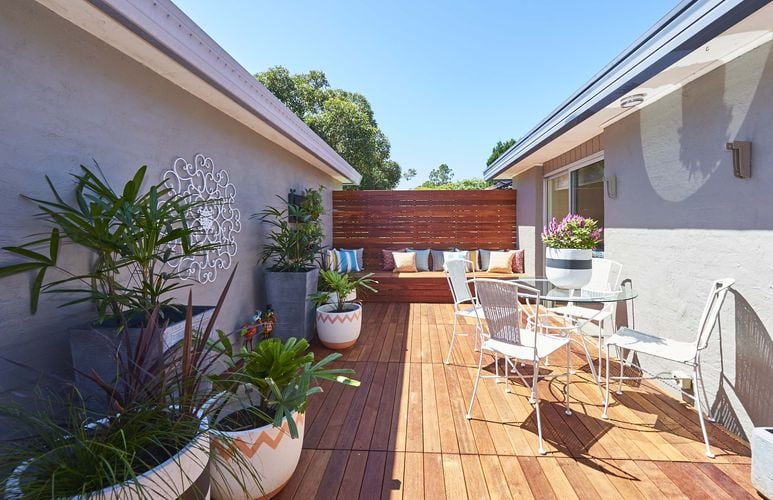 A bright summer outdoor deck with throw pillows and plants between two houses