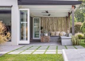 Covered outdoor patio with modern seating, ceiling fans, stepping stone pavers and landscaped lawn.