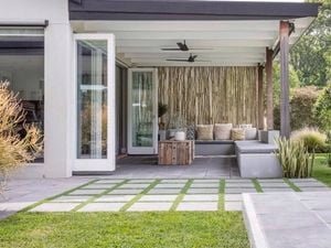 Covered outdoor patio with modern seating, ceiling fans, stepping stone pavers and landscaped lawn.